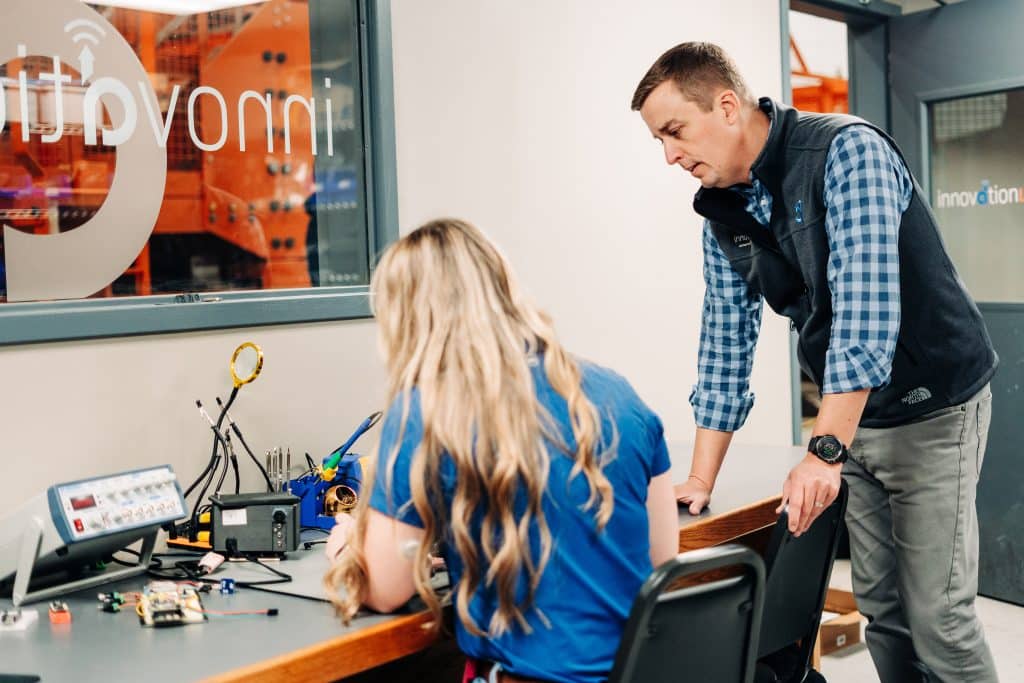 A man overseeing a woman working on technical equipment in a lab
