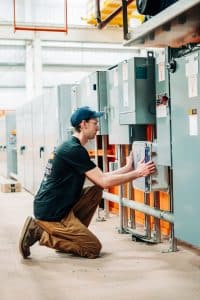 A man crouching down to install a piece of technology onto a large piece of manufacturing equipment