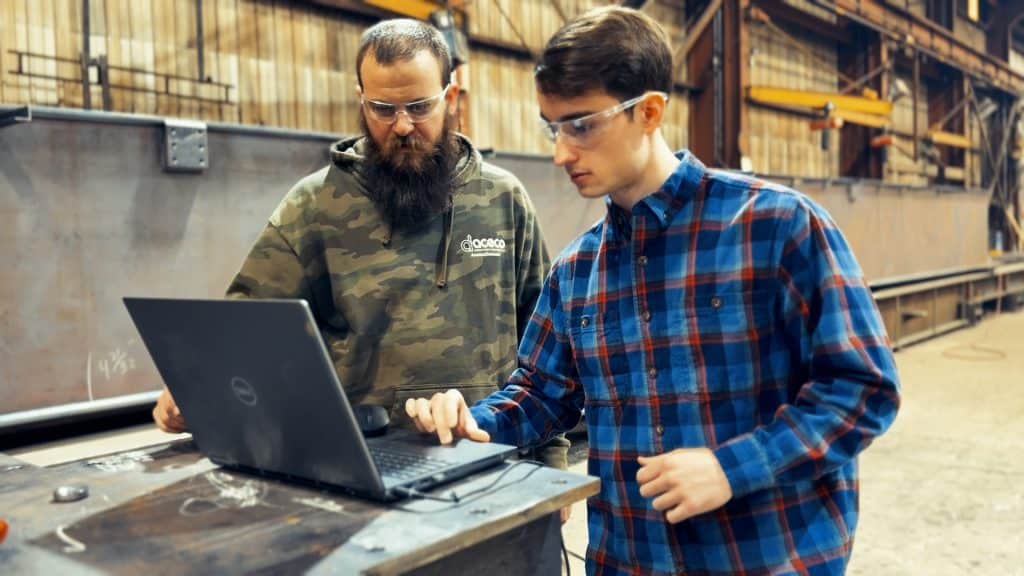 Two men working on a computer in a manufacturing shop
